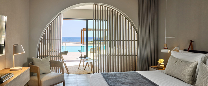 Die moderne Suite des Ella Elissa auf Rhodos öffnet sich durch eine elegante Bogenschiebetür zum Balkon. Von dort reicht der Blick über den Pool bis zum Meer.