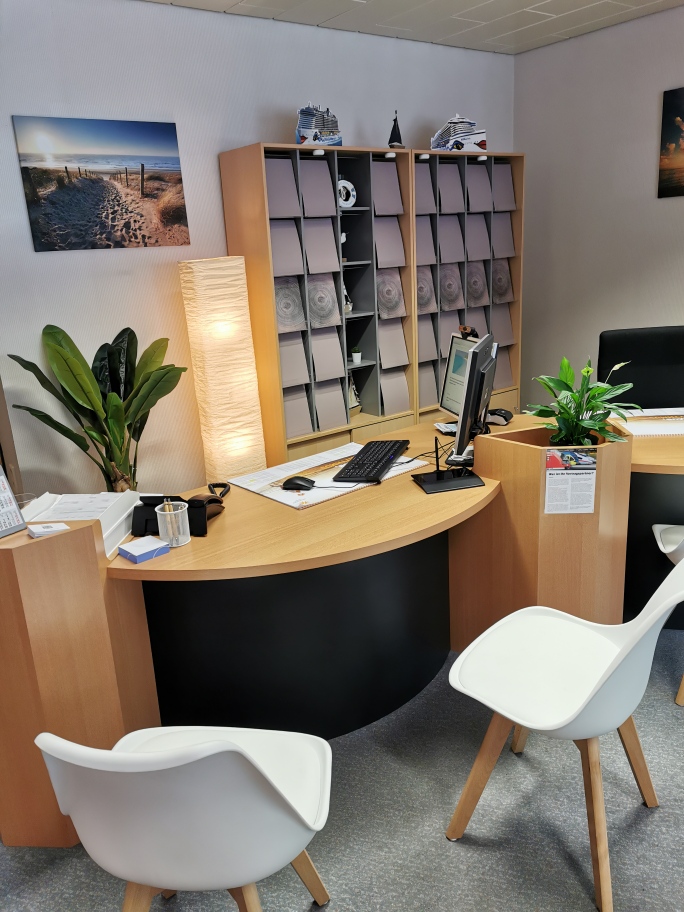 Foto eines Arbeitsplatzes mit 2 Kundenstühlen, Pflanze und Stehlampe und Regalwand im Hintergrund